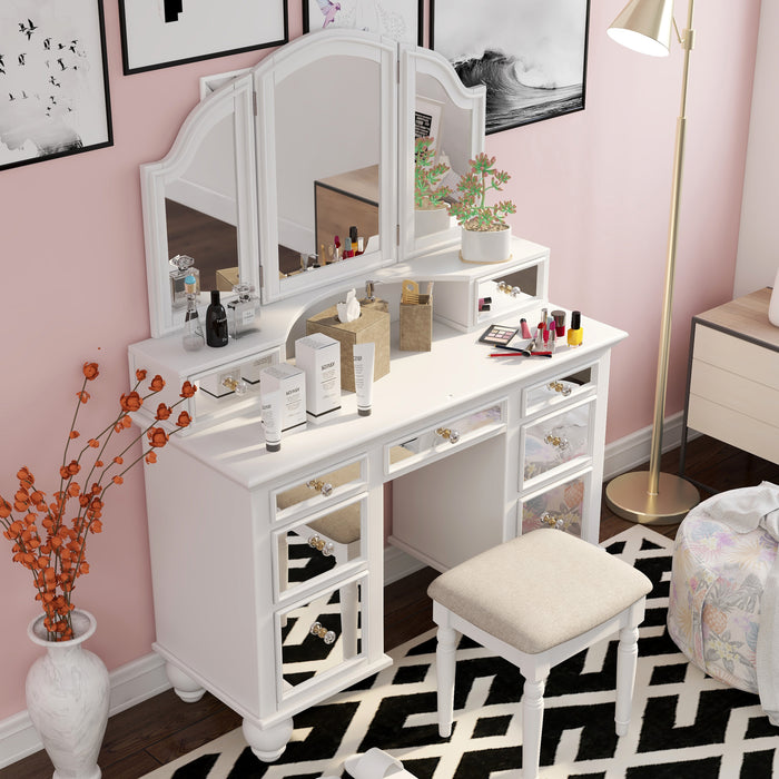 Top view of a white vanity set in a pink youth bedroom. Make-up and creams adorn the vanity table. The stool sits on a black and white patterned rug that ties in with the black-framed art surrounding the mirror. A gold floor lamp, on the right, shines a light on the vanity table.