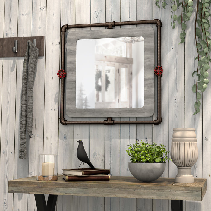 Left-angled industrial gray wood and pipe frame wall mirror with red accents over a console in a rustic living space
