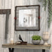 Left-angled industrial gray wood and pipe frame wall mirror with red accents over a console in a rustic living space