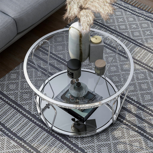 Right angled top-down modern round chrome steel coffee table with open teardrop shape legs and a tempered glass top and mirror open bottom shelf decorated with accessories on a rug.