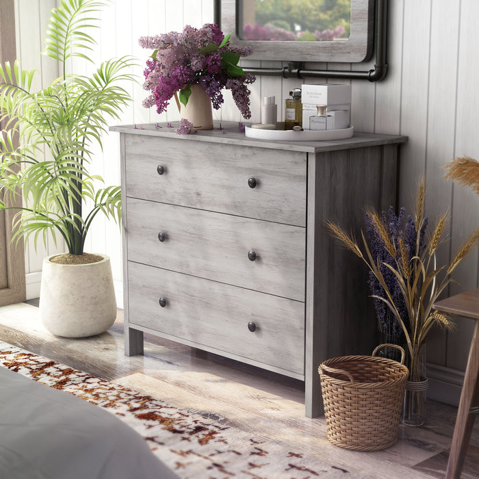 Left angled contemporary vintage gray oak three-drawer tall dresser in a bedroom with accessories
