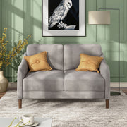 Front facing modern grey velvet loveseat with sloping arms in a room with accessories