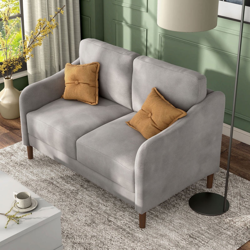 Left facing bird's eye view of a modern grey velvet loveseat with sloping arms in a room with accessories