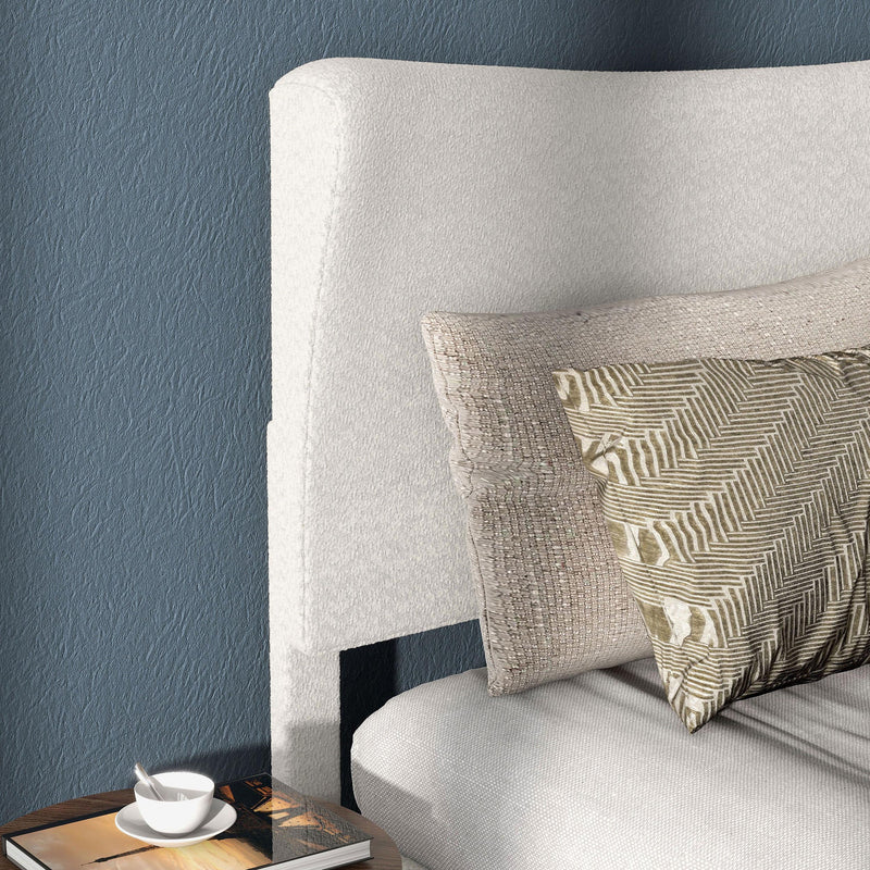 Right facing close up the headboard of a modern white boucle upholstered queen bed in a room with linens and accessories