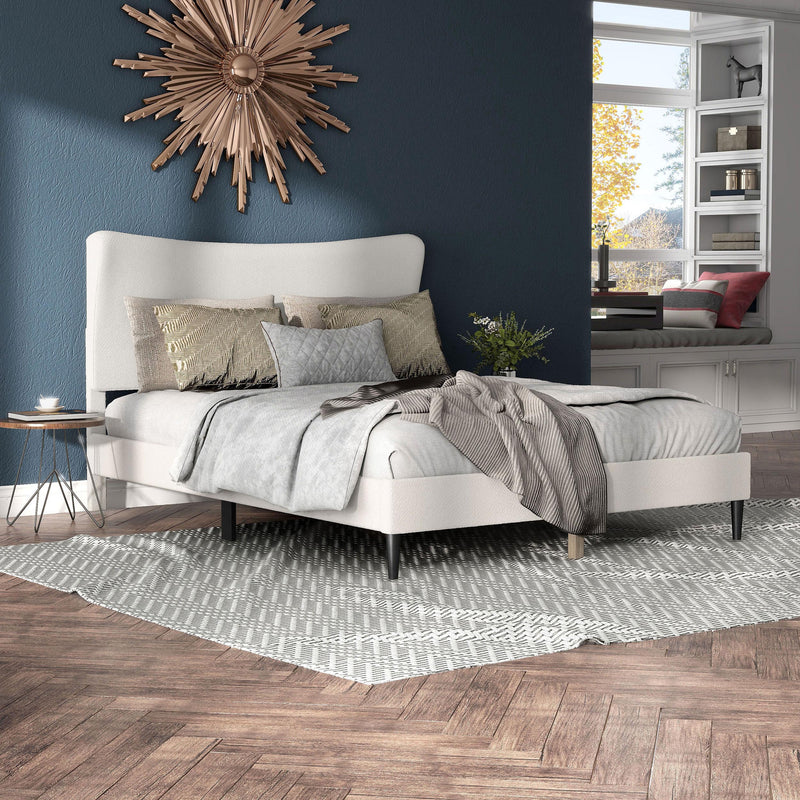 Right facing modern white boucle upholstered queen bed in a room with linens and accessories