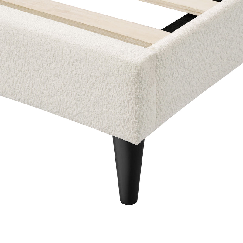 Left facing close up of the footboard corner and support leg of a modern white boucle upholstered queen bed on a white background