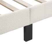 Left facing close up of the side rail, slats, and support leg of a modern white boucle upholstered queen bed on a white background