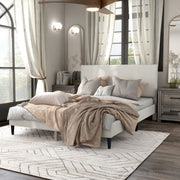 Left facing modern white boucle upholstered queen bed in a room with linens and accessories