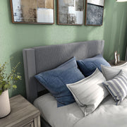 Right facing close up view of a modern gray velvet textured headboard queen platform bed in a room with linens and accessories