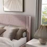 Left facing close up view of a modern pink velvet textured headboard full platform bed in a room with linens and accessories
