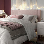 Left facing close up of a modern pink velvet textured headboard queen platform bed in a room with linens and accessories