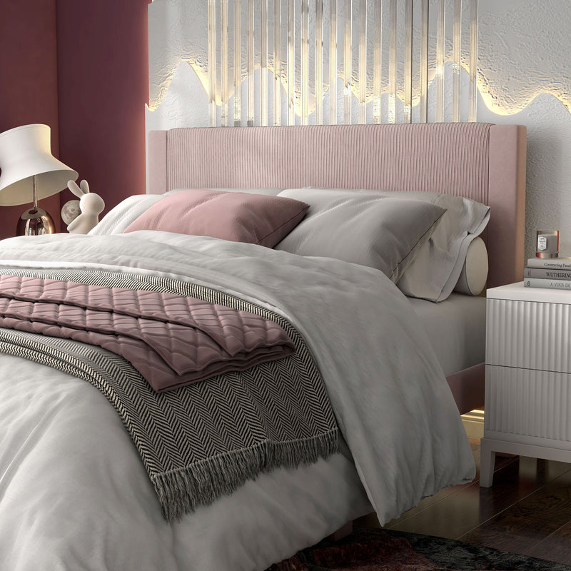 Left facing close up of a modern pink velvet textured headboard queen platform bed in a room with linens and accessories