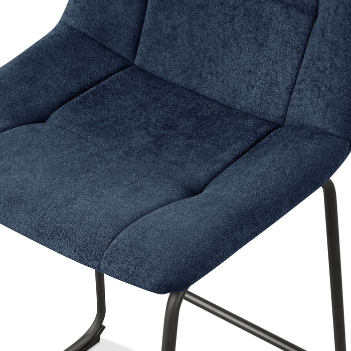 Left facing close up single view of the seat on a set of two contemporary blue chenille counter height stools with black bases on a white background