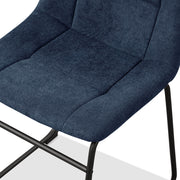 Left facing close up single view of the seat on a set of two contemporary blue chenille dining side chairs with black bases on a white background