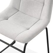 Left facing close up single view of the seat on a set of two contemporary light grey chenille dining side chairs with black bases on a white background