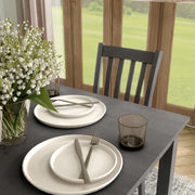 Side facing close up view of a five-piece traditional grey wooden dining set with a table and four chairs in a room with accessories