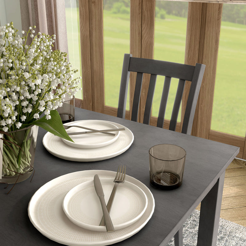Side facing close up view of a five-piece traditional grey wooden dining set with a table and four chairs in a room with accessories