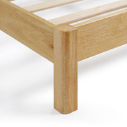 Right facing close up corner leg view of a modern wood frame queen platform bed with a channel tufted upholstered white boucle headboard on a white background