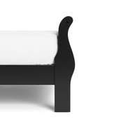 Right facing close up side view of a traditional black finish solid wood queen sleigh bed showing its footboard, on a white background