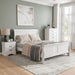 Right facing three-piece traditional white finish solid wood queen bedroom set with (1) queen sleigh bed, (1) two-drawer nightstand, and (1) five-drawer chest in a room with linens and accessories