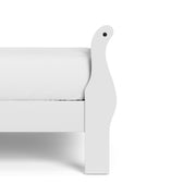 Right facing close up side view of a traditional white finish solid wood queen sleigh bed showing its footboard, on a white background