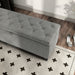 Left facing bird's eye close up of a modern grey upholstered storage bench with a lift top in a room with accessories
