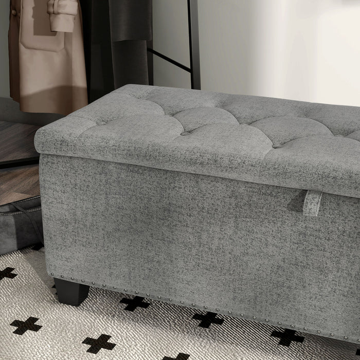 Left facing close up of a modern grey upholstered storage bench with a lift top in a room with accessories
