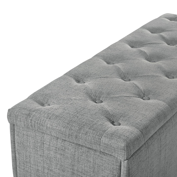 Right facing close up of a modern grey upholstered storage bench with a lift top on a white background