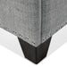 Right facing close up of the nailhead trim and leg of a modern grey upholstered storage bench with a lift top on a white background