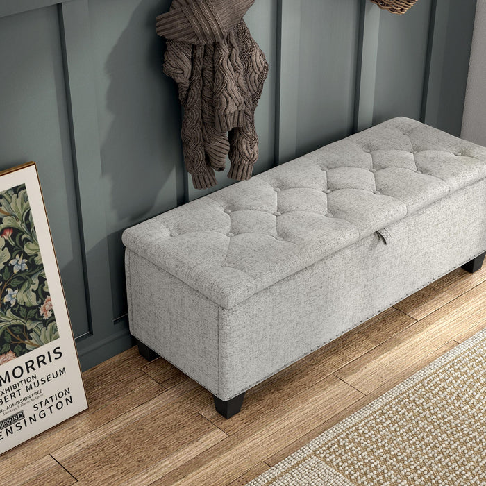 Right facing bird's eye close up of a modern off white upholstered storage bench with a lift top in a room with accessories