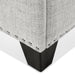 Right facing close up of the nailhead trim and leg of a modern off white upholstered storage bench with a lift top on a white background