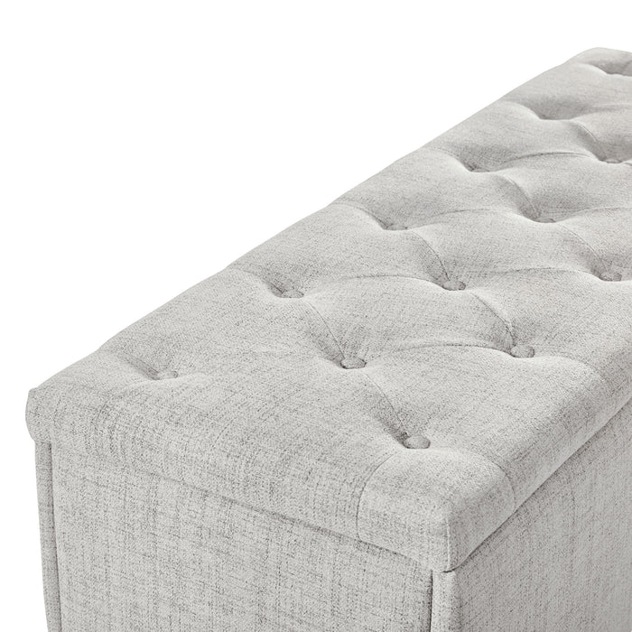 Right facing close up of the tufted top of a modern off white upholstered storage bench with a lift top on a white background