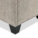 Right facing close up of the nailhead trim and leg of a modern light brown upholstered storage bench with a lift top on a white background