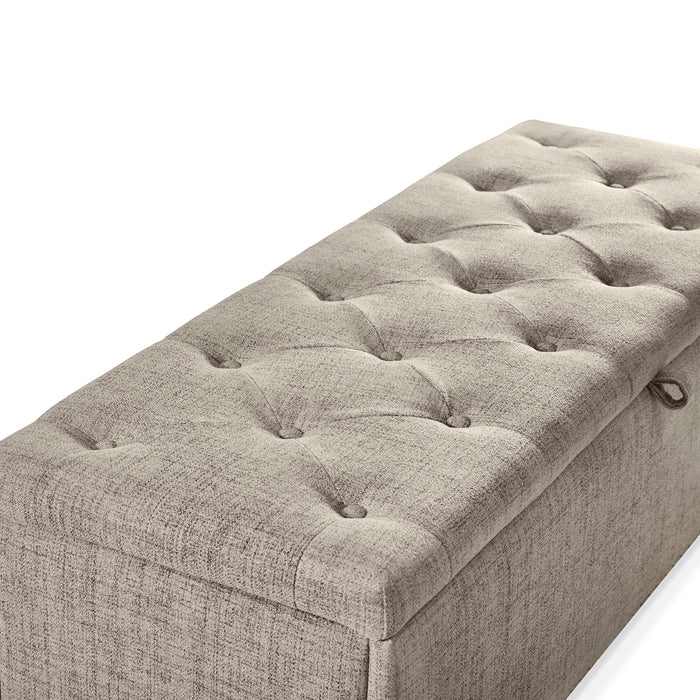 Right facing close up of the tufted top of a modern light brown upholstered storage bench with a lift top on a white background