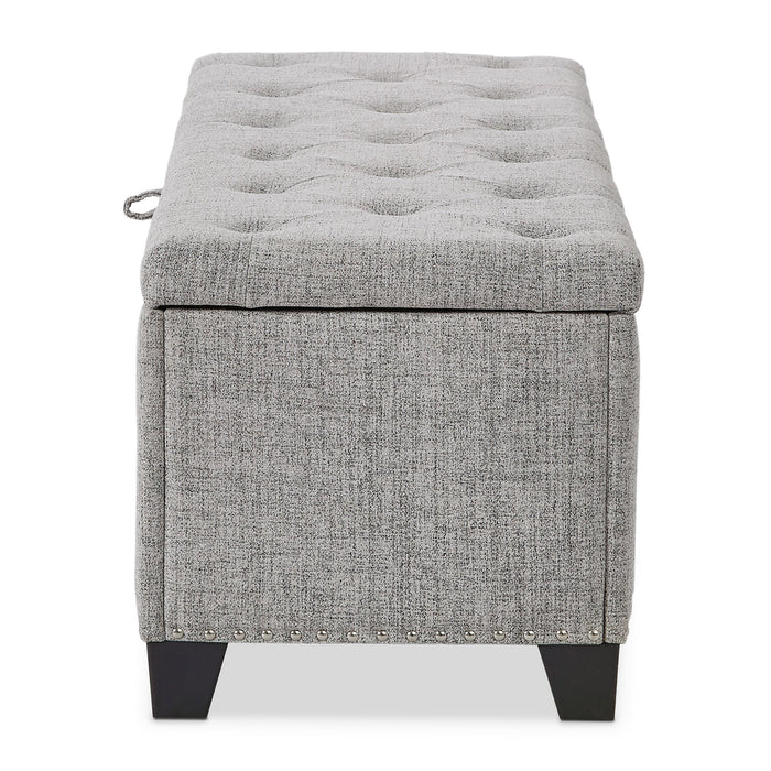 Front facing side view of a modern light grey upholstered storage bench with a lift top on a white background