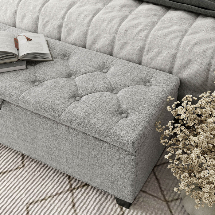 Left facing close up of the tufted top of a modern light grey upholstered storage bench with a lift top in a room with accessories