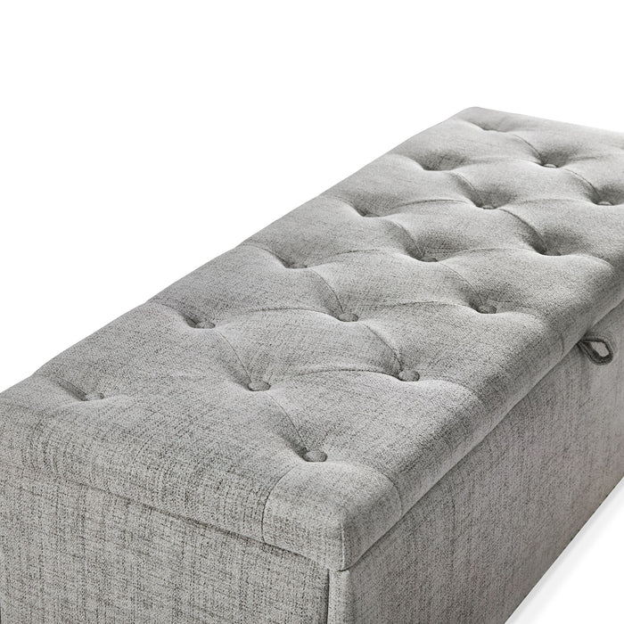 Right facing close up of the tufted top of a modern light grey upholstered storage bench with a lift top on a white background