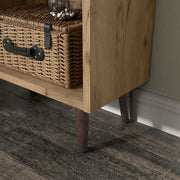 Left facing close up of the leg of a mid-century modern light oak two-drawer tall bookcase in a room with accessories