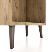 Right facing close up of the leg of a mid-century modern light oak two-drawer tall bookcase on a white background