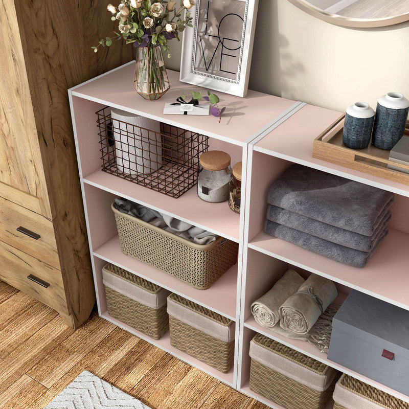 Left facing high camera view of a durable modern three-shelf light pink storage bookcase in a larger modular configuration in a room with accessories