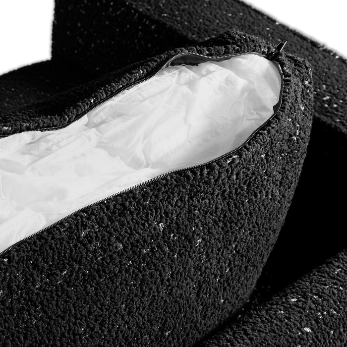 Right facing close up of the zippered pillow cover of a contemporary black and metallic boucle loveseat on a white background