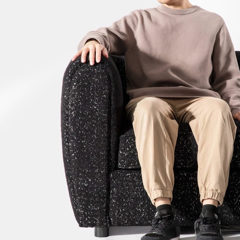Front facing close up of a contemporary black metallic boucle shelter armchair with a person seated on a white background