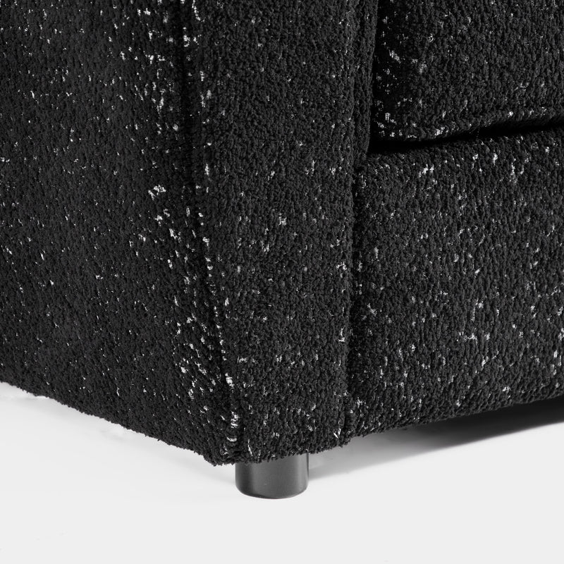 Right facing close up of the leg of a contemporary black metallic boucle shelter armchair on a white background