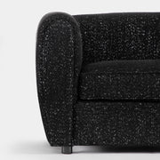 Front facing close up of the rounded armrest of a contemporary black metallic boucle shelter armchair on a white background