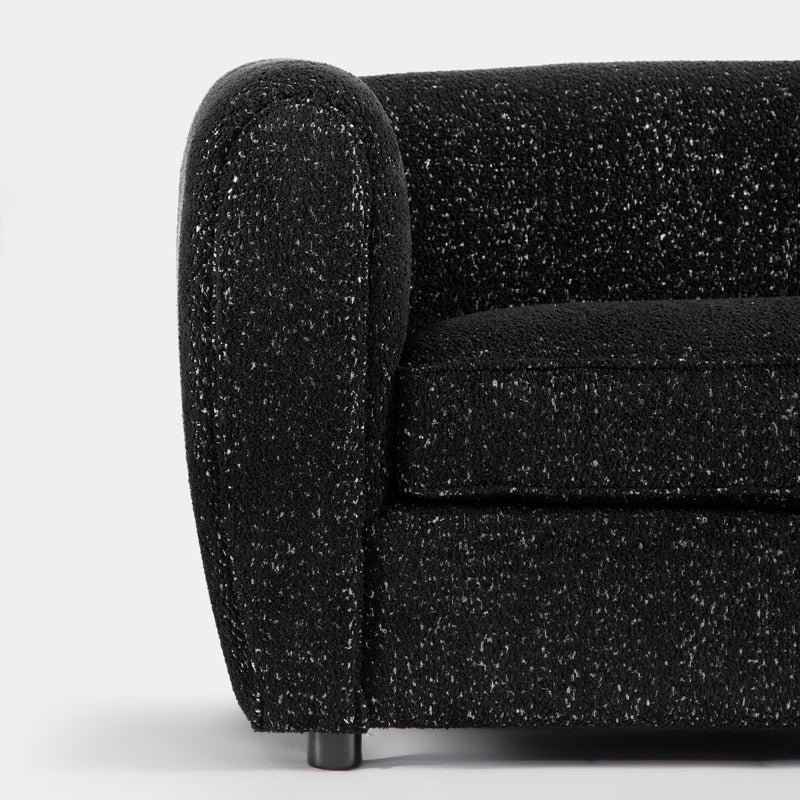 Front facing close up of the rounded armrest of a contemporary black metallic boucle shelter armchair on a white background