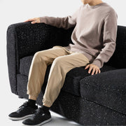 Left facing close up of a contemporary black metallic boucle shelter sofa with a person seated on a white background
