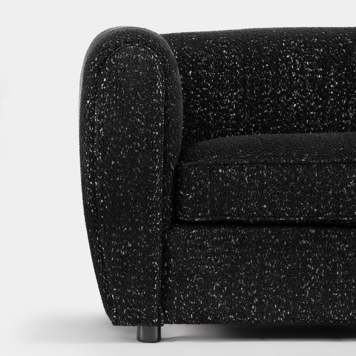 Front facing close up of the rounded armrest of a contemporary black metallic boucle shelter sofa on a white background