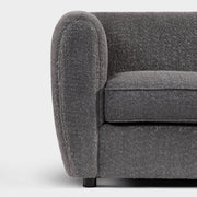 Front facing close up of the armrest and leg of a contemporary charcoal gray metallic boucle shelter armchair on a white background