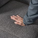 Left facing close up of a person's hand pressing into the seat cushion of a contemporary charcoal gray metallic boucle shelter loveseat
