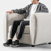 Left facing close up of a person seated on a contemporary off-white metallic boucle shelter armchair on a white background